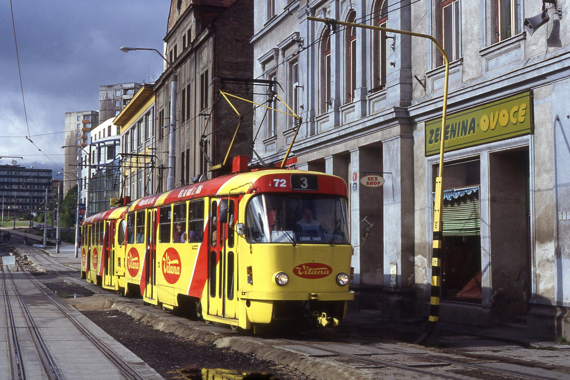 Psal se rok 1995 a přestavba tramvajových tratí v libereckém dolním centru byla v plném proudu. Liberecká souprava 72/73 se proto zvolna kolébá po provizorní kolejiv ulici 1. máje a míří na Soukenné náměstí a dál do Lidových Sadů. Z budovy "Uranu" v pozadí sice již dávno zmizelo heslo hlásající že "Náš uran slouží míru", nicméně fasády domů dosud připomínají, v jakémže ráji jsme si tu žili... Půvabným dokumentem živelných změn je "SEX SHOP" umístěný hned vedle prodejny ZELENINA OVOCE 😀 (archiv M.Fogl)